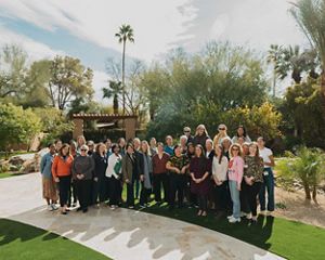 A group of women gather for a group photo outside at an event.