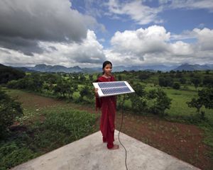 A woman stands outside and holds up a solar panel.