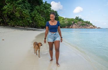 Woman walks on beach with dog.