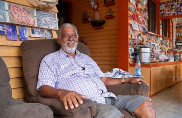 Man smiles as he sits on armchair, books behind him.