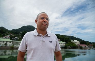 Man stands near harbor, homes in background.