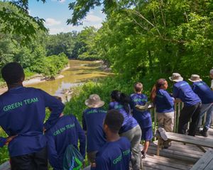A group of teenagers wearing matching blue t-shirts, lined up along a wooden deck, overlooking a river in the summer.