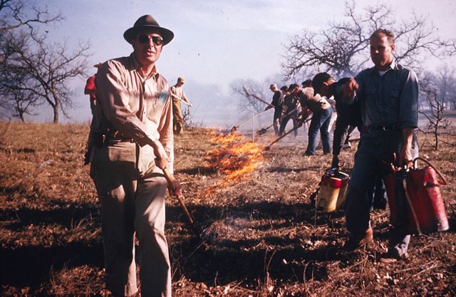 A historic photo of several men tending to a fire in a grassland.