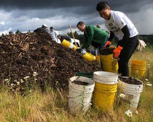 Smiling volunteers with buckets bending over a pile of dirt.