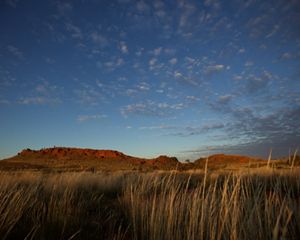 Red mountains are viewed from grassy plains.
