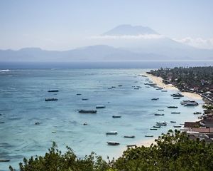 an expansive view of an Indonesian island's coastline with fishing boats and a tall mountain on the horizon