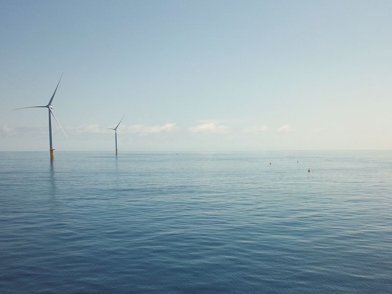 small boat on still sea with offshore wind turbines in distance.