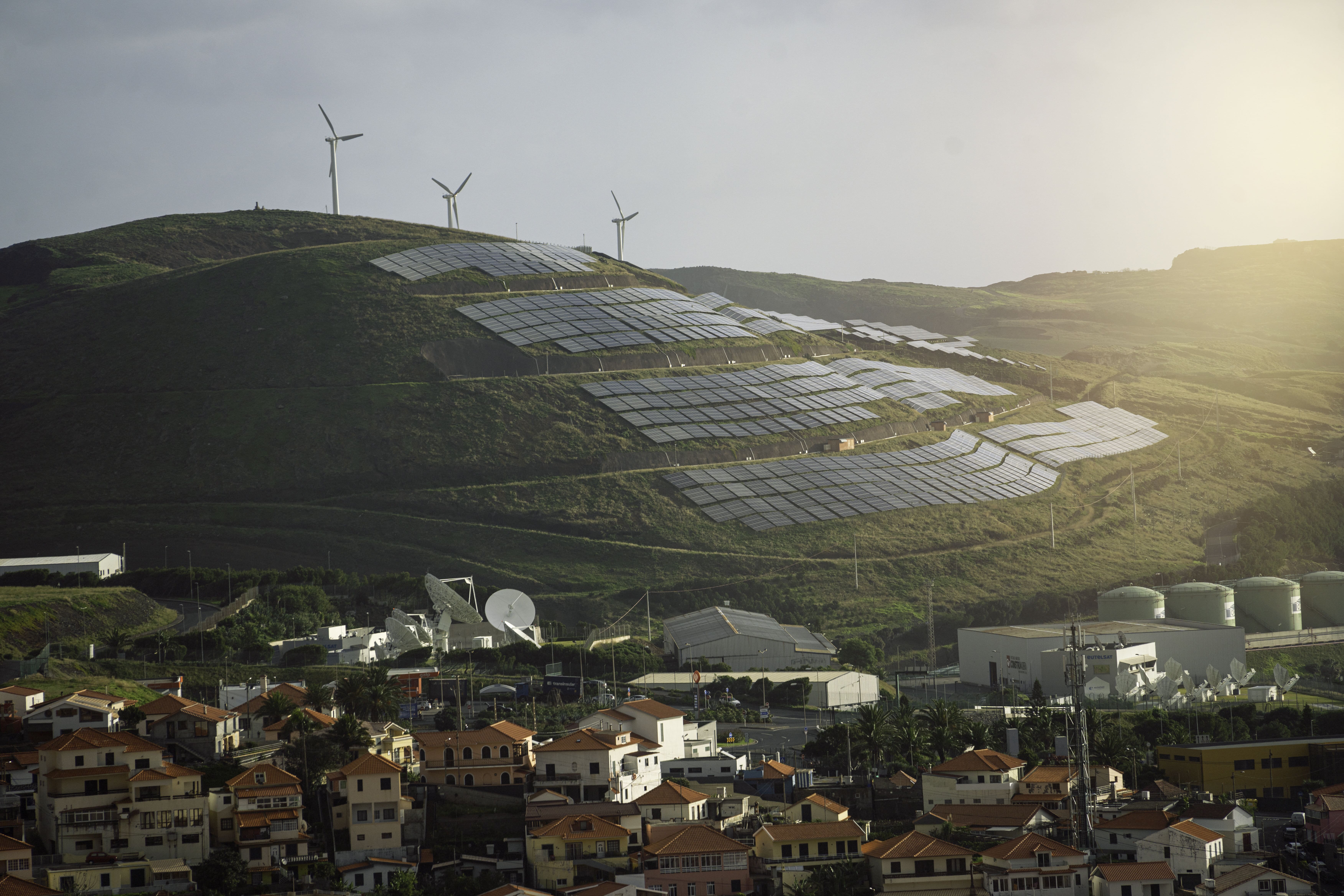 solar panels and wind turbines on a hill above village.