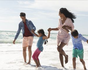 A family holding hands running along the beach.