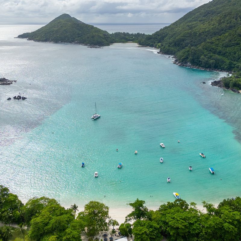 Aerial view of a Seychelles harbor, with beach, boats and islands in background.