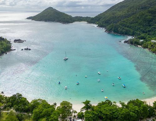 Aerial view of a Seychelles harbor, with beach, boats and islands in background.