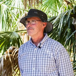 Alejandro Fierro stands beneath shady palm trees.