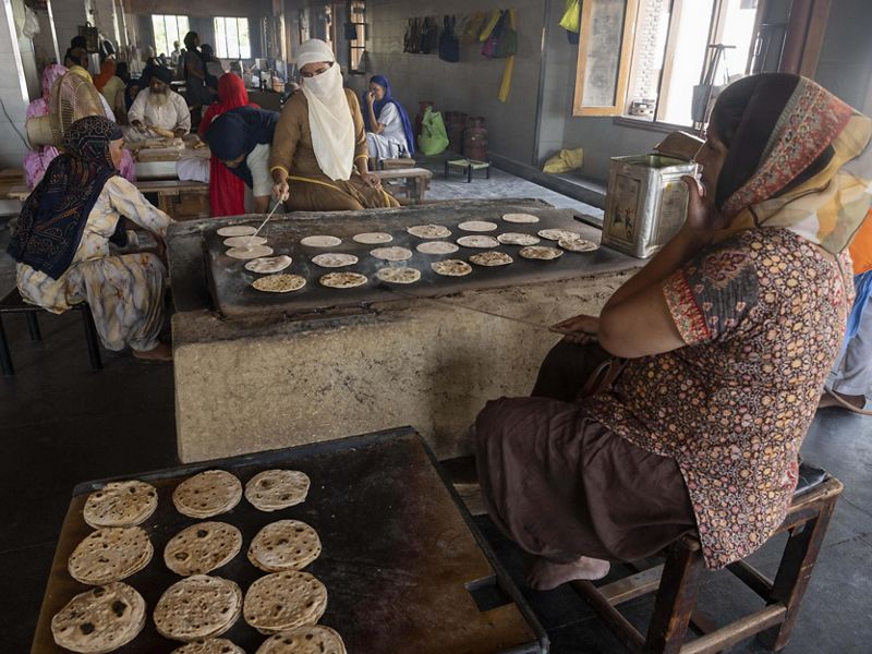 A woman tends to dozens of flat breads on a large stove as other community members work in the background.