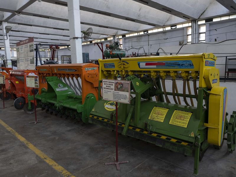 In a long university building, three large seeder machines of different colors sit next to each other, full of rotors and hoses.