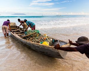 men pushing a small wooden boat filled with fishing nets.