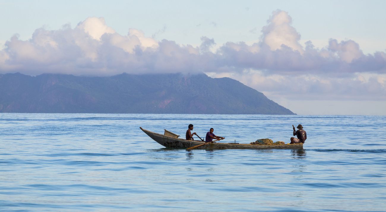 3 people in a wooden canoe in the open water.