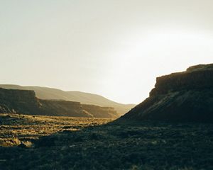 The face of a mesa sits in darkness as the sun glows behind it, filling the desert valley with light.