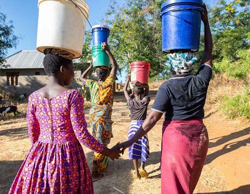 A group of women with buckets on their heads walking away.